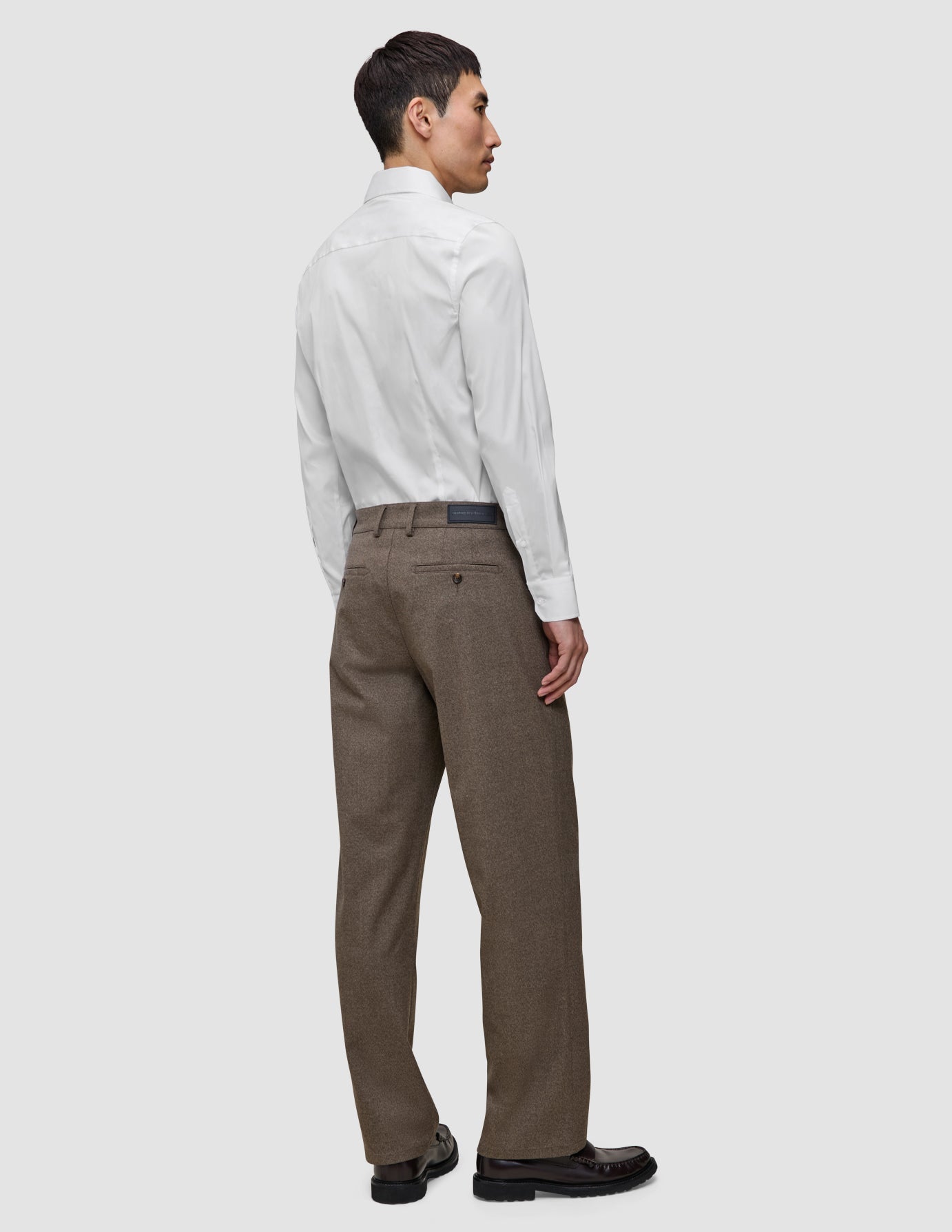 En man som står längst bak, klädd i en vit, smal Elevated-skjorta instoppad i bruna byxor och svarta loafers.